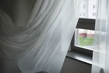 Białe firanki falujące przy oknie. Dowiedz się, jak doprać pożółkłe firanki domowym sposobem, żeby były śnieżnobiałe.