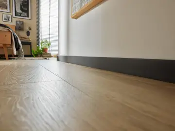 Nowoczesne wnętrze z jasną podłogą i ciemnymi dębowymi listwami przypodłogowymi, które podkreślają elegancję pomieszczenia.
