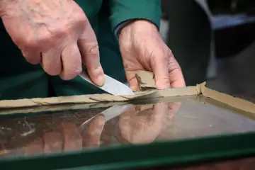 Ręce nakładają kit do okien drewnianych na szybę, przygotowując ją do montażu.