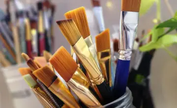 Un pot rempli de pinceaux aux poils orangés, prêts à être utilisés avec un nettoyant peinture acrylique.
