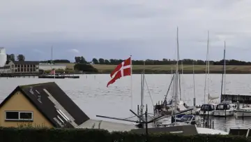 Dania graniczy z Niemcami. Flaga Danii powiewa nad portem pełnym żaglówek.