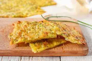 Schiacciata di zucchine dorata e croccante, con erbe aromatiche, servita su un tagliere di legno.