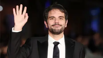 Valerio Vestoso saluta con la mano, sorridendo con un abito elegante.