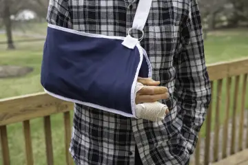 Mężczyzna w kratę z ręką w temblaku. Uraz ręki, który może być objęty ubezpieczenie kl.
