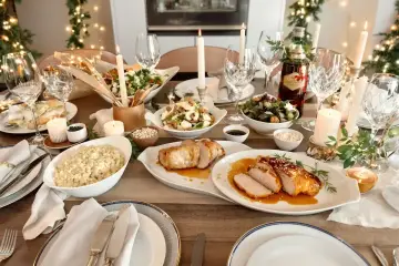 Mesa de Nochevieja con carnes asadas, ensaladas, velas y luces festivas.