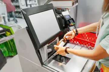 Kasa samoobsługowa: skutki automatyzacji handlu a zatrudnienie. Klient skanuje butelkę, zastanawiając się nad przyszłością pracy kasjerów.