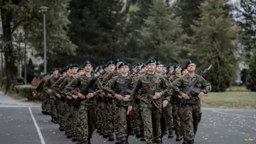Żołnierze w zielonych beretach i mundurach maszerują w zwartym szyku. W rękach trzymają karabiny, gotowi do służby w swoim pułku.