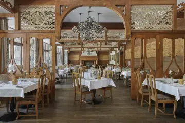 Elegancka restauracja w stylu góralskim, idealna dla hoteli 5 gwiazdkowych. Drewniane zdobienia, kryształowy żyrandol i nakryte stoły tworzą przytulną atmosferę.