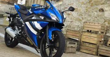 Niebieski sportowy motocykl Yamaha R25, idealny jako pierwszy motor na kat B, stoi na bruku obok drewnianych skrzynek.