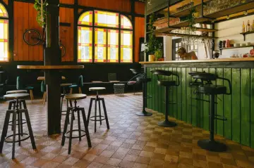 Wnętrze kawiarni z zielonym barem, stołkami i rowerem na ścianie. Idealne miejsce na coffee ride.