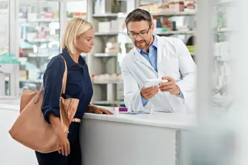 Farmaceuta w białym kitlu pokazuje klientce opakowanie leku, być może na aspargan.