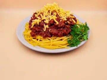 Prosty przepis na spaghetti z mięsem mielonym: makaron z sosem bolońskim, posypany startym serem i udekorowany natką pietruszki.