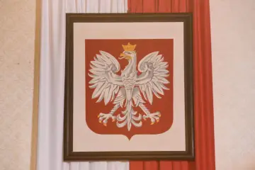 Obraz przedstawia godło Polski – białego orła w koronie na czerwonej tarczy. Dzieło oprawione w ciemną ramę, zawieszone między biało-czerwonymi zasłonami.