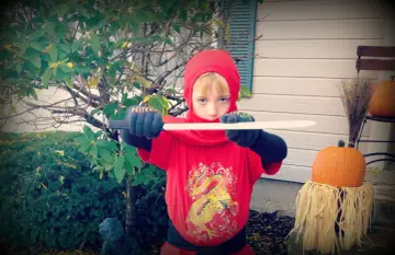Chłopiec w czerwonym stroju ninja z mieczem, gotowy do akcji. To świetny pomysł, jak zrobić strój ninja na Halloween!