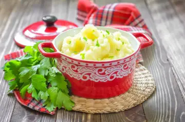 Purée ziemniaczane w czerwonej misce, ozdobione natką pietruszki, na drewnianym stole.