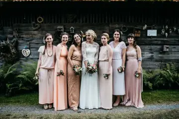 Brautjungfern in zarten Pastelltönen posieren vor rustikaler Holzwand, ein Bild von einer entspannten boho hochzeit.