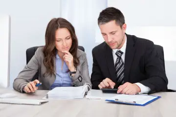 Dos profesionales concentrados revisan documentos y utilizan una calculadora para contabilizar facturas de años anteriores.