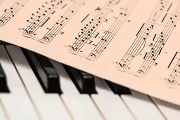 Partytura muzyczna leży na klawiaturze fortepianu. Widać nuty i cyfry, jakby ktoś przygotowywał się do zagrania "alleluja".