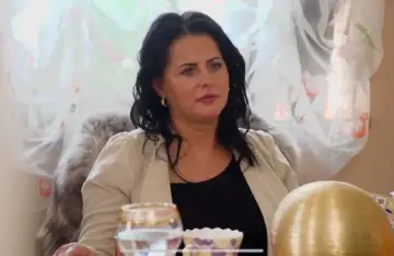Edzia, królowa życia, w eleganckim żakiecie, siedzi przy stole.