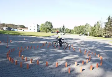 Młody rowerzysta w kamizelce odblaskowej i kasku pokonuje tor przeszkód z palików, przygotowując się do egzaminu na kartę rowerową.