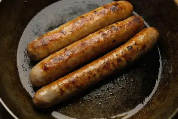 Drei goldbraune Bratwürste brutzeln in einer Pfanne. Perfekt für leckere Bratwurst Rezepte!