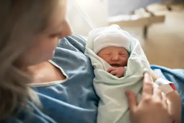 Mama tuli dziecko, które śpi otulone kocykiem. To piękny moment, który może być wspierany przez zasiłek rodzicielski.