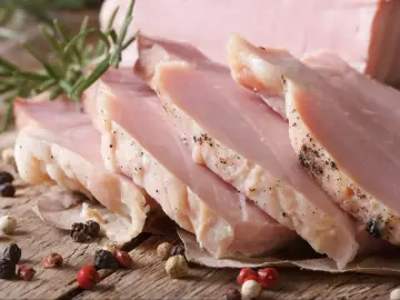 Pokrojony, **super delikatny i soczysty schab gotowany**, przyprawiony pieprzem, z gałązką rozmarynu na drewnianym blacie.