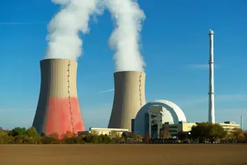 Dwie chłodnie kominowe elektrowni jądrowej z parą unoszącą się w niebo. W tle kopuła reaktora i wysoki komin.