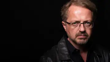 Przemysław Borkowski z Kabaretu Moralnego Niepokoju w czarnej skórzanej kurtce i okularach, zamyślony.