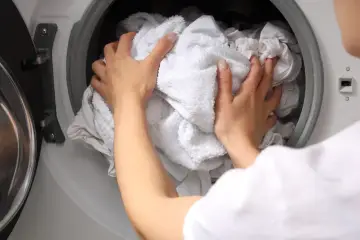 Ręce wkładają białe pranie do pralki. Dowiedz się, dlaczego białe ubrania szarzeją po kilku praniach i jak temu zapobiec.