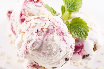 Pyszne lody z mascarpone z malinami i kawałkami białej czekolady, udekorowane listkiem mięty.
