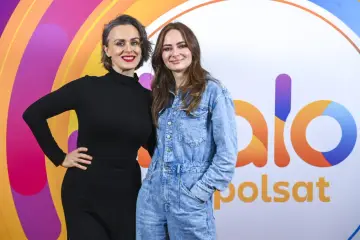 Ania Rusowicz, córka Niemena, w czarnej sukience i dżinsowym kombinezonie pozuje na tle logo Polsat.
