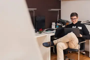Uśmiechnięty mężczyzna na stażu pracuje przy laptopie. Czy po zakończeniu stażu pracodawca musi zatrudnić?
