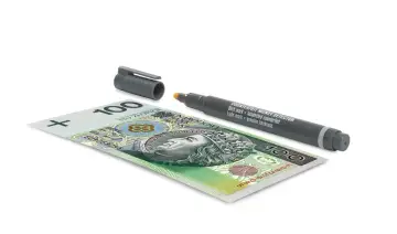 Banknot 100 zł obok pisaka do wykrywania fałszerstw. Pisak z napisem "COUNTERFEIT MONEY DETECTOR" sugeruje, że zaraz sprawdzimy autentyczność banknotu.