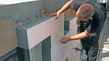 Budowlaniec montuje płyty styropianowe do ocieplenia domu. Wybór odpowiedniego styropianu to klucz do energooszczędności.