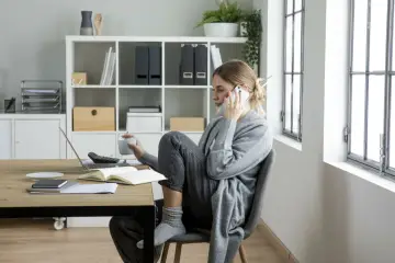 Kobieta rozmawia przez telefon, trzymając kubek. Na biurku laptop, notatnik i kalkulator. Czy to oznaka stagnacji, co to znaczy dla jej pracy?