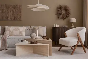 Salon w stylu japandi: beżowa sofa, puszysty fotel, kamienne stoliki i dekoracje z traw.