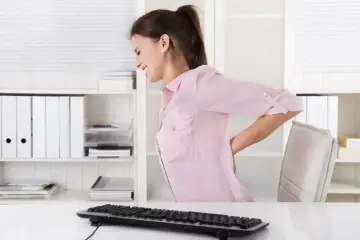 Kobieta w biurze odczuwa ból pleców, objaw choroby zawodowej.