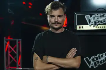 Wiktor Dyduła, z charakterystycznym wąsem i tatuażem węża, prezentuje swoje utwory na scenie Voice of Poland.
