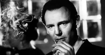 Liam Neeson jako Oskar Schindler, z papierosem w dłoni, w kadrze z filmu "Lista Schindlera".