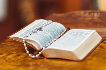 Otwarta Biblia, na której leży różaniec. Widoczny jest tekst Ewangelii św. Mateusza.