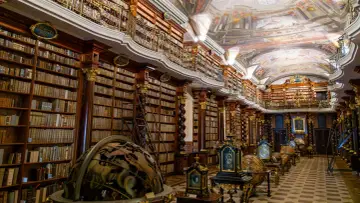 Wnętrze Biblioteki Narodowej Republiki Czeskiej z bogato zdobionymi regałami, globusami i malowanym sufitem.