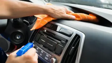 En hand sprayar och torkar av bilens instrumentbräda med en orange trasa. Det ser ut som en magisk rengöring för att få bilen skinande ren.