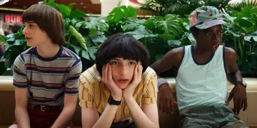Trzech chłopców z Stranger Things 3 siedzi obok siebie, otoczonych bujną zielenią.