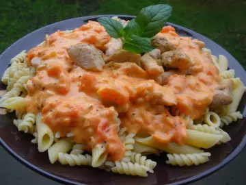 Penne i fusilli z kurczakiem w kremowym sosie pomidorowym z mascarpone, udekorowane listkiem bazylii.