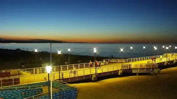 Wieczorny spacer po molo na jelitkowo plaży. Zachodzące słońce maluje niebo, a latarnie oświetlają ścieżkę.