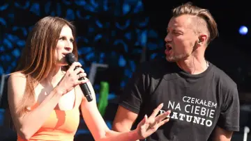 Sylwia Grzeszczak i Liber na scenie, wokalistka śpiewa do mikrofonu, a raper w koszulce z napisem "Czekałem na Ciebie Piątunio" energicznie gestykuluje.
