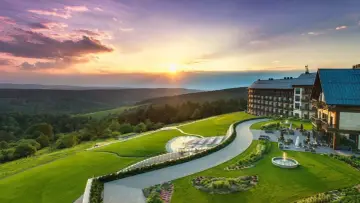 Hotel Arłamów z basenem i tarasem, otoczony zielonymi wzgórzami o zachodzie słońca. Ile pokoi ma hotel Arłamów? Tego nie widać, ale jest ich wiele!