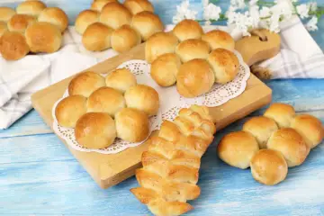 Morbidi panini al latte dorati, alcuni disposti a grappolo su un tagliere, altri su un panno bianco.