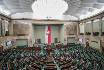 Sala sejmowa z rzędami zielonych foteli, gdzie partie polityczne debatują nad przyszłością kraju.